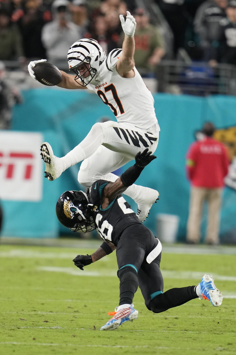 Cincinnati Bengals tight end Tanner Hudson (87) leaps over Jacksonville Jaguars safety Antonio Johnson (26) during the second half of an NFL football game, Monday, Dec. 4, 2023, in Jacksonville, Fla. (AP Photo/John Raoux)