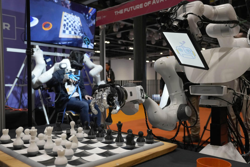 A robot performs the action of the human in background to play chess during the International Conference on Robotics and Automation ICRA in London, Tuesday, May 30, 2023. The 2023 ICRA brings together the world's top academics, researchers, and industry representatives to show the newest developments. Team NimbRo from the University of Bonn, Germany, has designed this avatar system that can be controlled by humans. (AP Photo/Frank Augstein)