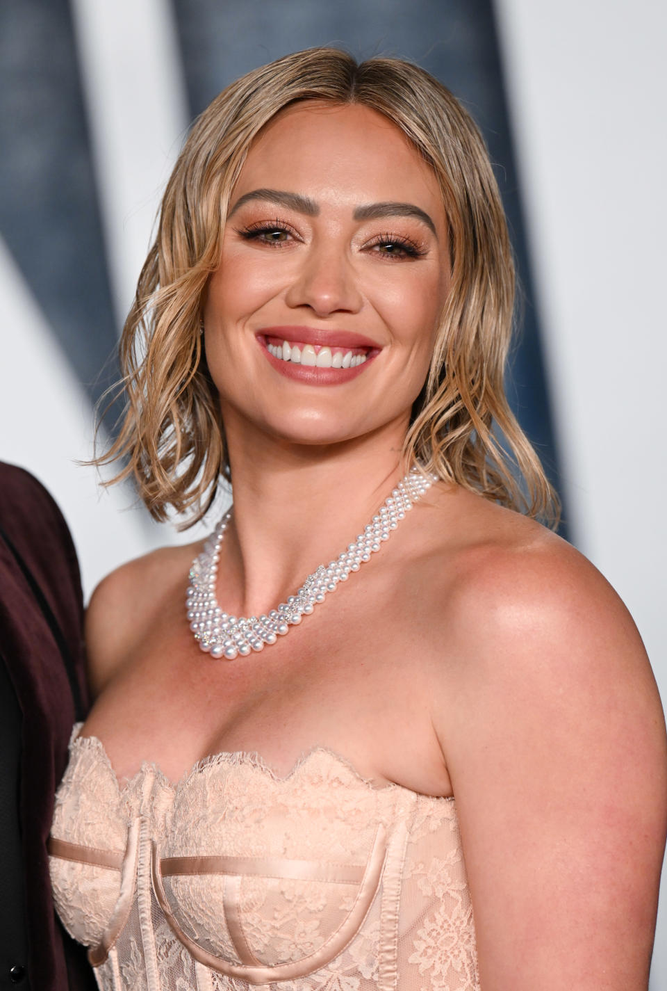 Hilary Duff smiles on the red carpet in a strapless corset-style gown and layered pearl necklace.