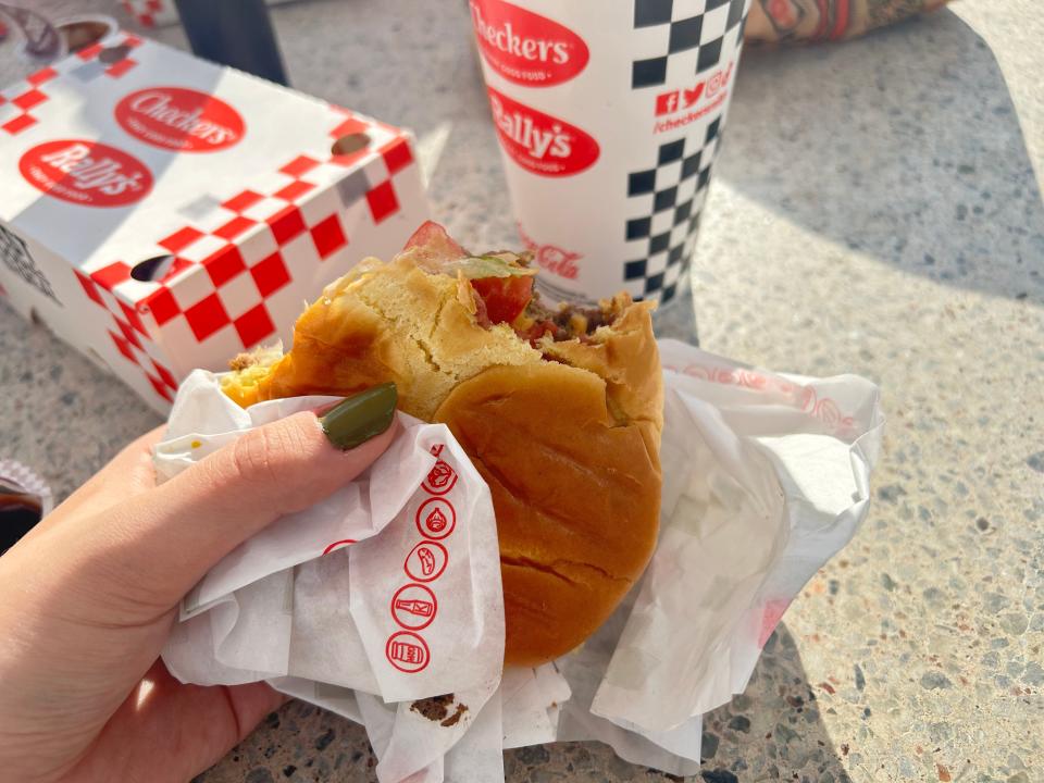 hand holding up a cheeseburger in front of a box and a cup from checkers