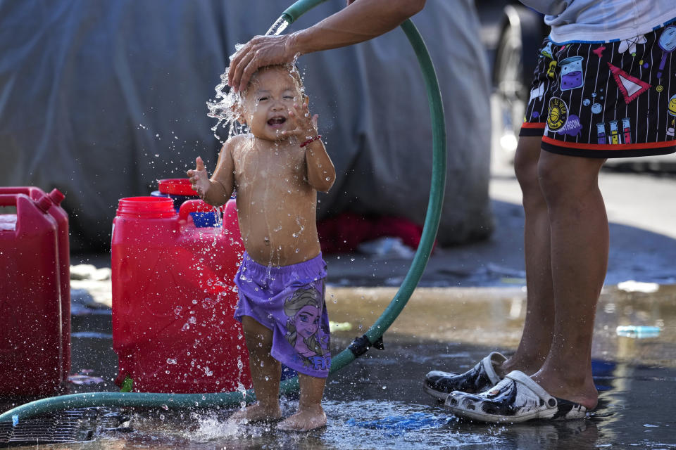 A man pours water on his daughter on a hot summer day in Manila, Philippines on Friday, April 26, 2024. (AP Photo/Aaron Favila)