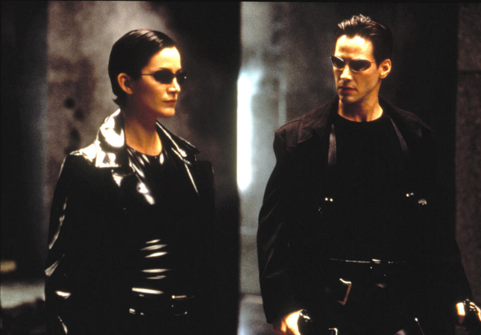 Characters Trinity and Neo stand side-by-side in 'The Matrix', wearing signature black leather outfits