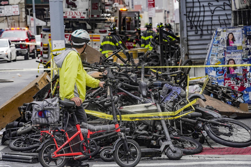 A biker stops to look at a pile of e-bikes in the aftermath of a fire in Chinatown, which authorities say started at an e-bike shop and spread to upper-floor apartments, Tuesday June 20, 2023, in New York. (AP Photo/Bebeto Matthews)