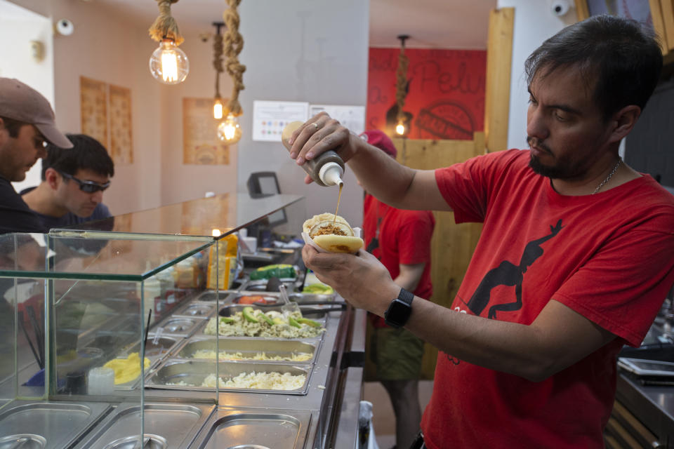 In this June 19, 2019 photo, chef and owner of the Arepa Ole restaurant, Edgar Rodriguez from Venezuela, prepares an Iberia Arepa with Serrano ham, tomato and olive oil, in Madrid, Spain. Rodriguez became one of the earliest ambassadors of the food when he fled to Spain over a decade ago and opened up an arepa restaurant. He now has several fusion items on the menu including Spanish staples like serrano ham. (AP Photo/Paul White)