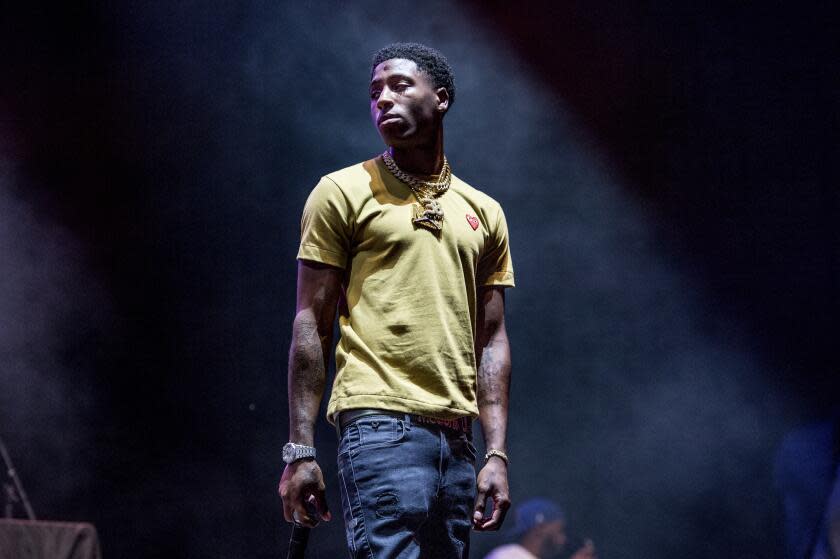 A young Black man in a yellow shirt and jeans standing with hands on his side on a stage