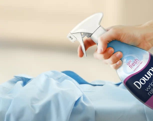 A model's hand spraying the wrinkle release spray on a blue Oxford cloth shirt