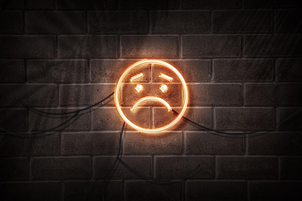 a neon wall art piece of a sad emoji with downturned eyebrows and a downturned mouth