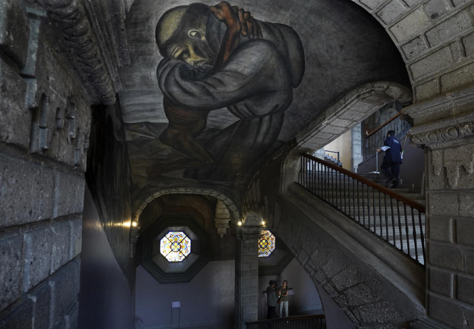 A mural by Jose Clemente Orozco titled, "Franciscans" and depicting a friar embracing an Indigenous man, adorns the ceiling, vault and side of a stairwell, inside the former Jesuit college Antiguo Colegio de San Ildefonso in Mexico City, Wednesday, April 26, 2023. Divine figures and religious references can frequently be found in the murals at San Ildefonso because religion became a key part of the cultural identity of the country after the Spanish conquest, an expert says. (AP Photo/Marco Ugarte)