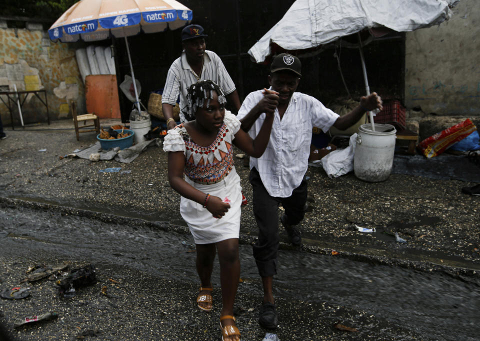 A Haitian couple jumps over running wastewater in Port-au-Prince, Haiti, Friday, July 9, 2021, two days after Haitian President Jovenel Moise was assassinated in his home. (AP Photo/Fernando Llano)