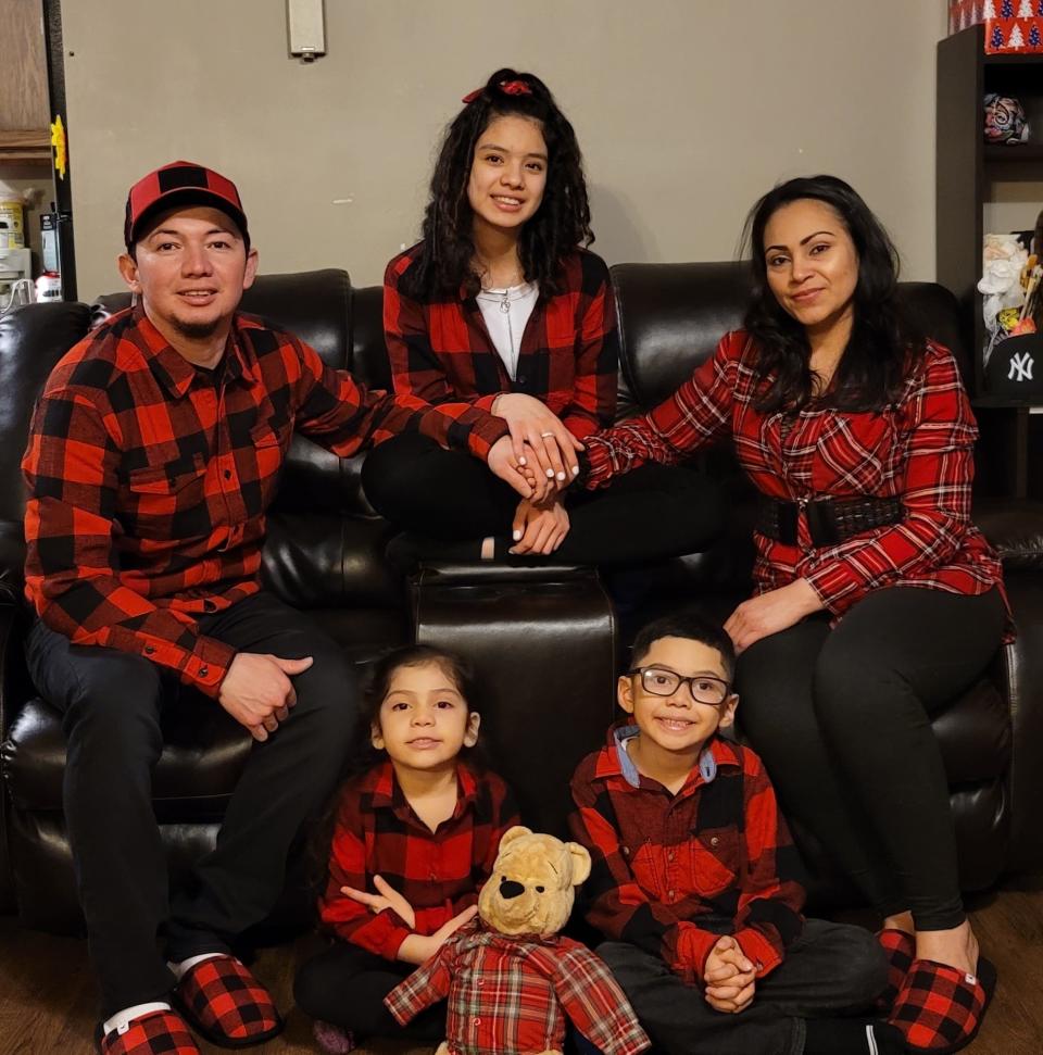 The Hernandez-Pinto family wearing red plaid shirts sitting on the couch smiling at the camera.