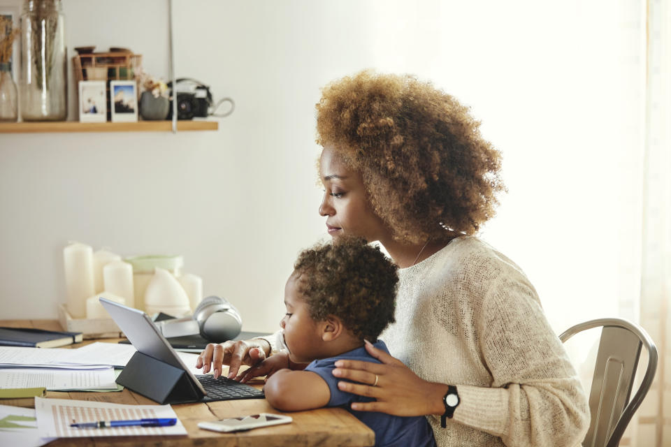 careers Boy looking at mother using digital tablet. Woman sitting with son at table in kitchen. She is working from home.