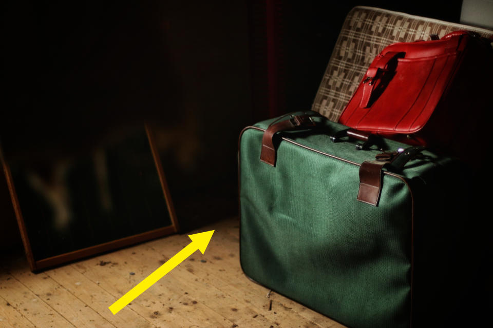 Green suitcase and red briefcase on a wooden floor next to a chair and a leaning mirror