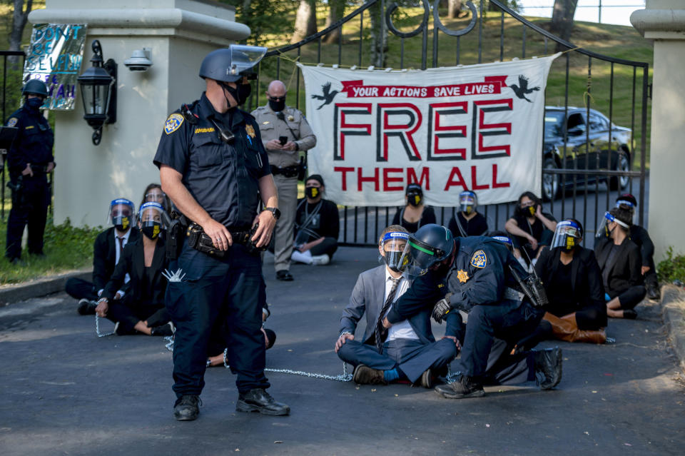 FILE - In this July 27, 2020, file photo, a California Highway Patrol officer inspects a chained protester who was part of a group calling for mass prison inmate releases outside of California Gov. Gavin Newsom's mansion in Fair Oaks, Calif. California state prison officials say in a recent court filing that as many as 17,600 inmates are eligible for release due to the coronavirus, 70% more than previously estimated and a total that victims and police say includes dangerous criminals who should stay locked up. (Daniel Kim/The Sacramento Bee via AP, File)