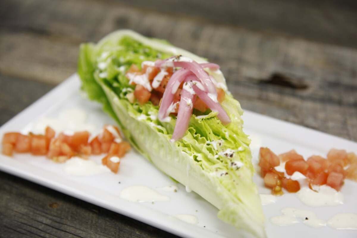 Closeup of a vegan salad bite on a white rectangle plate with tomato garnish with a blurred background of a rustic wooden table