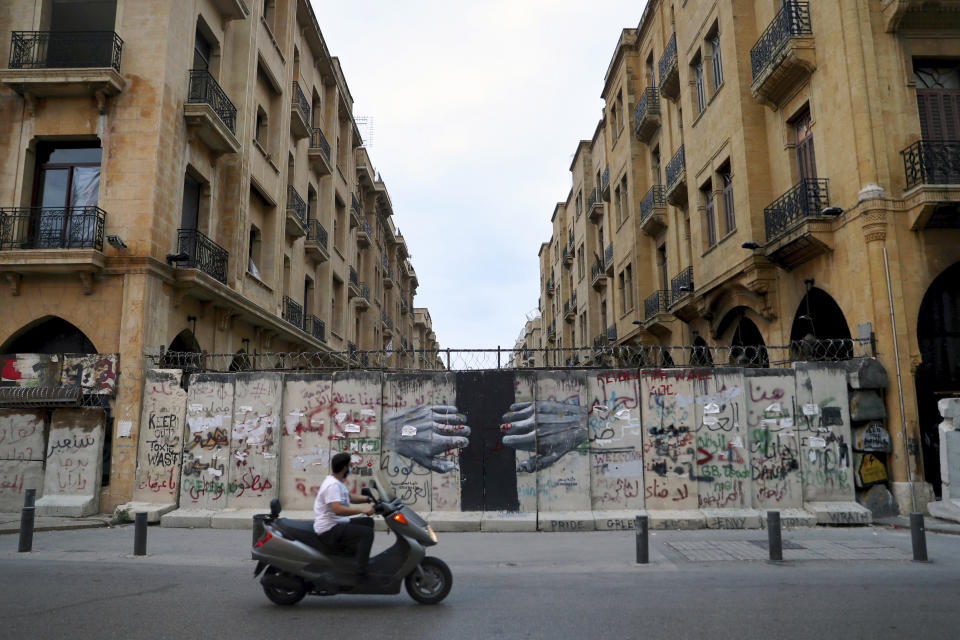 A man rides his scooter pasts a concrete wall that installed by security forces to don't let the anti-government protesters reach the parliament building, in downtown Beirut, Lebanon, Monday, Oct. 12, 2020. A year ago, hundreds of thousands of Lebanese took to the streets in protests nationwide that raised hopes among many for a change in a political elite that over that decades has run the country into the ground. (AP Photo/Bilal Hussein)