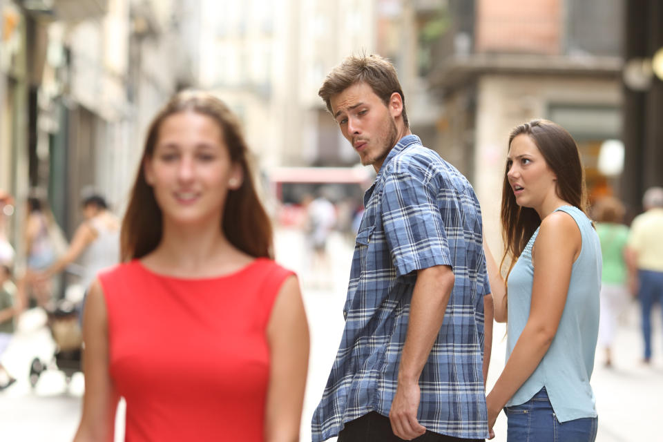 A man turning to look at a woman walking by while holding hands with another woman