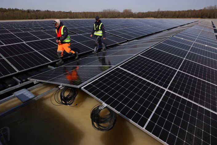 Workers walk along solar panels on a floating photovoltaic power plant on a lake.