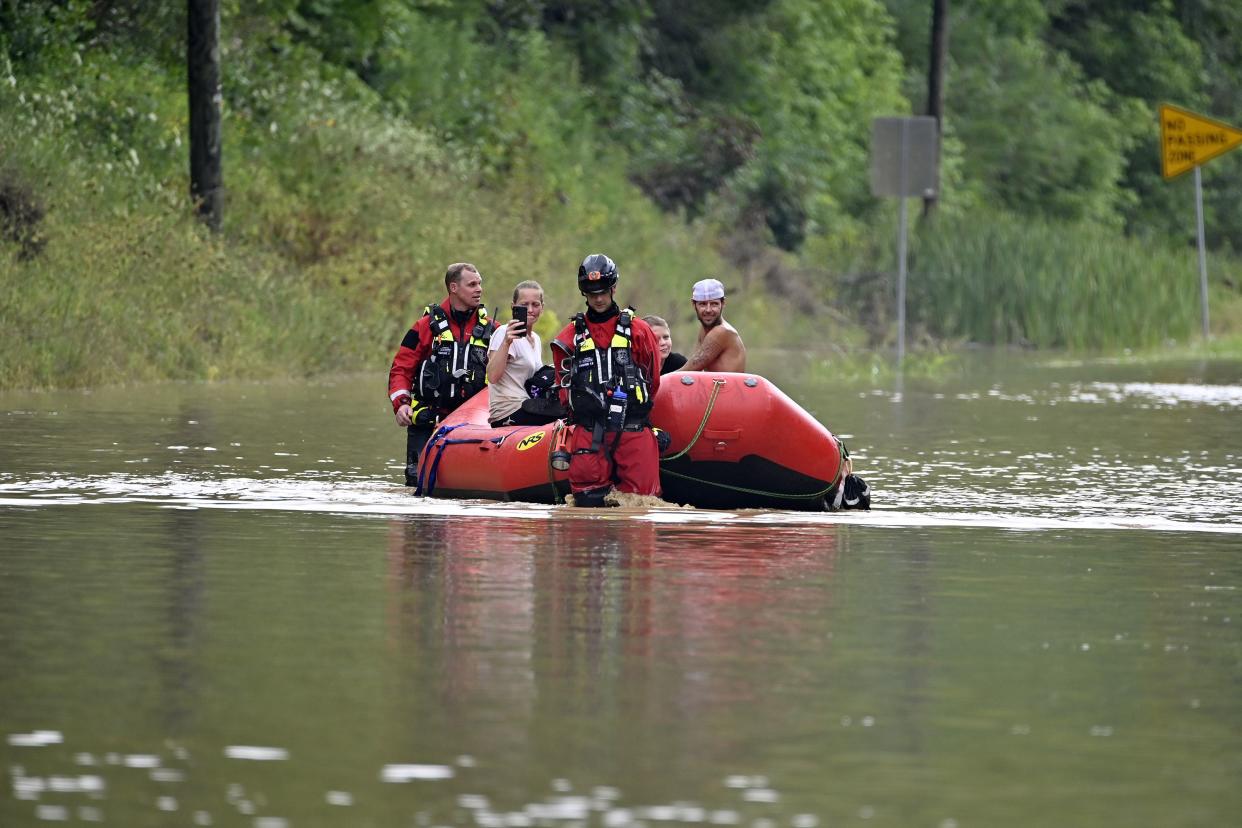 Members of the Winchester, Ky. Fire Department walk inflatable boats across flood waters over a road in Jackson, Ky. to pick up people stranded by the floodwaters on Thursday, July 28, 2022. The same stubborn weather system caused intense downpours in St. Louis and Appalachia that led to devastating, and in some cases deadly, flooding.