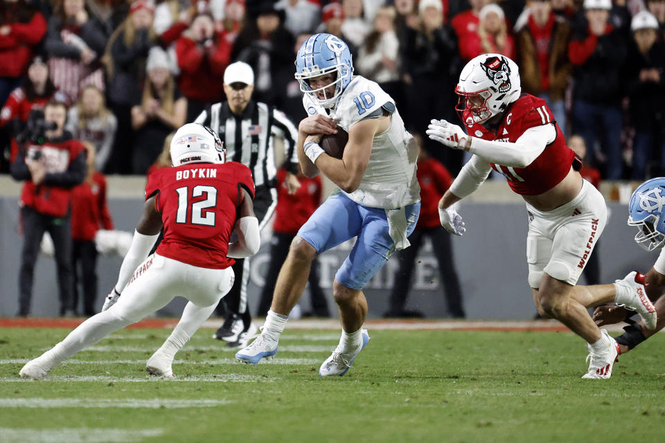 North Carolina's Drake Maye (10) tries to run the ball between North Carolina State defensive back Devan Boykin (12) and linebacker Payton Wilson (11) during the first half of an NCAA college football game in Raleigh, N.C., Saturday, Nov. 25, 2023. (AP Photo/Karl B DeBlaker)