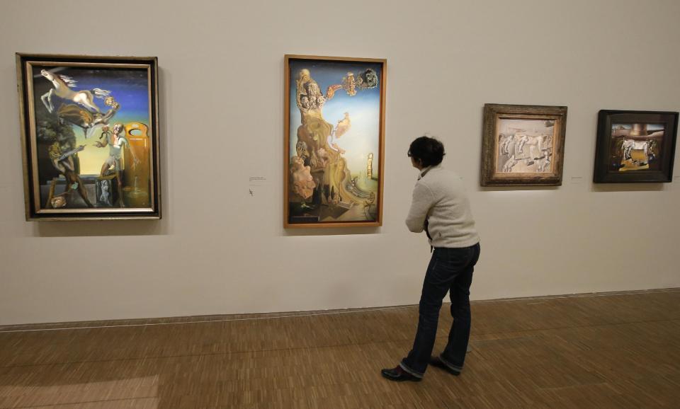 In this photo taken Monday Nov. 19, 2012, a woman looks at the painting 'La memoire de la femme enfant, 1929', second left, by Spanish artist Salvador Dali (1904-1989) during the presentation to the press of the exhibition "Dali" at the Centre Pompidou modern art museum, in Paris. A major retrospective of Salvador Dali in Paris aims to rewrite the art history books, reconciling for the first time the last decades of his life _ when he was accused of money-making self-publicity through numerous television appearances _ with his earlier, respected Surrealist period. (AP Photo/Francois Mori)