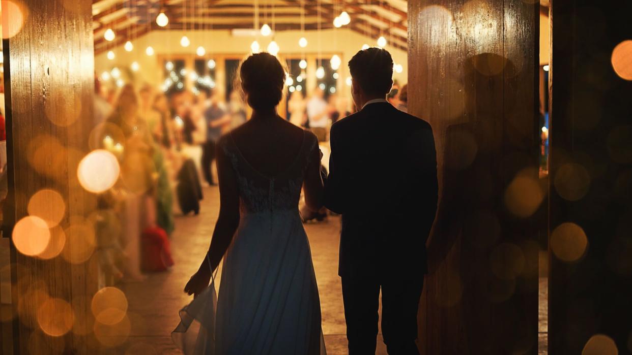 Rearview shot of a young couple arriving hand in hand at their wedding reception.