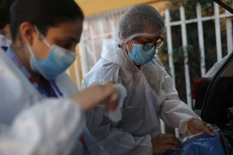 Foto de la médica venezolana Norelis Portal (D) y la técnica en enfermería chilena Blanca Pimente poniendose sus trajes protectores antes de visitar la casa de un paciente con coronavirus en Santiago