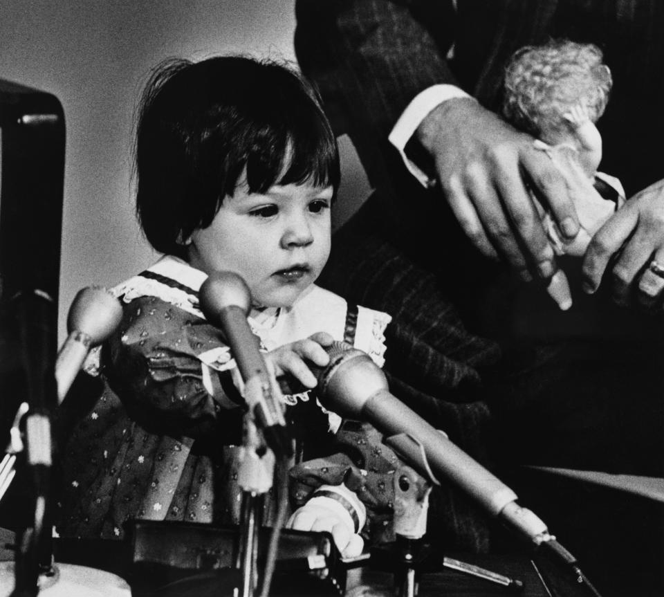 Elizabeth Carr as a baby, playing with microphones during a news conference. 