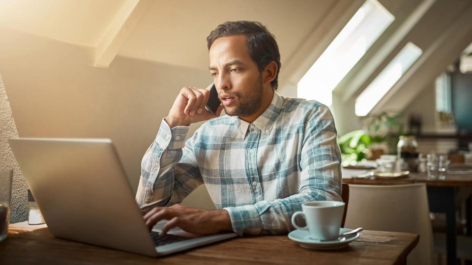 Shot of a young man talking on his phone while using his laptop.