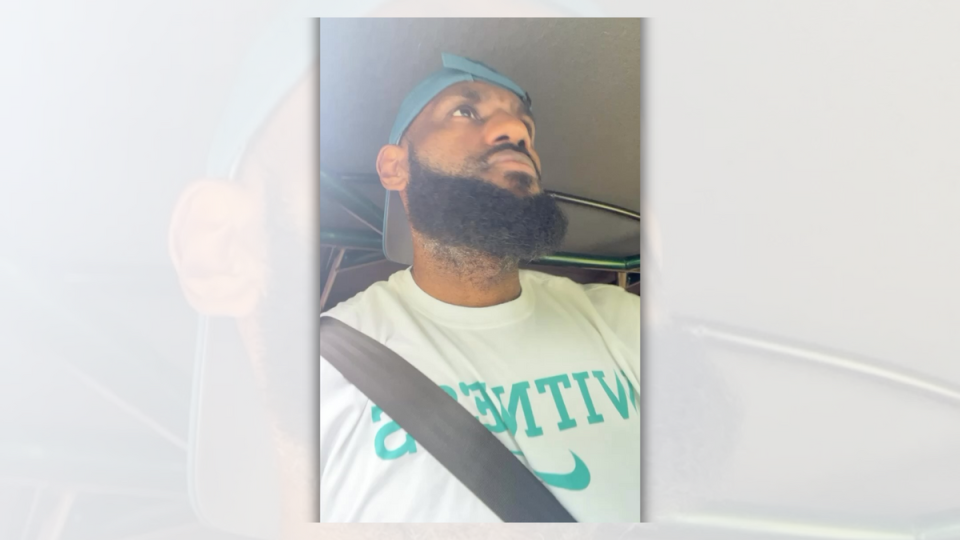 A Black man wearing a backwards blue hat is in a vehicle looking up towards the road. @kingjames/Instagram