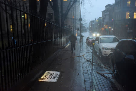 A man runs past tree limbs and debris scattered on the sidewalk as heavy rain and gusting winds from Storm Grayson cause disruptions in Halifax, Nova Scotia, Canada January 4, 2018. REUTERS/Darren Calabrese
