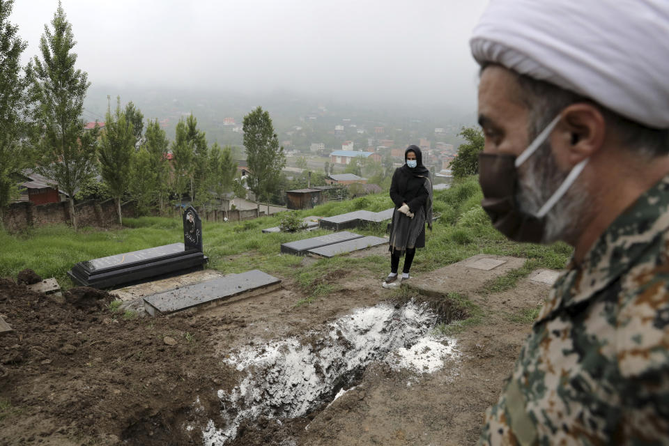 A woman wearing mask and gloves, prays on the grave of her mother who died from the coronavirus, at a cemetery in the outskirts of the city of Babol, in north of Iran, Thursday, April 30, 2020. (AP Photo/Ebrahim Noroozi)