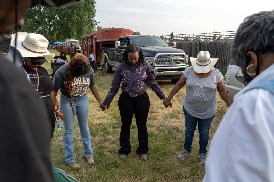 Staci Russell, 39, center, of Belleville, lowers her head as her family, including her mother, Pam Russell, right, of Canton, and her goddaughter/cousin Kennedy Ervin, 14, of Oak Park, hold hands in prayer for Russell before she takes part in the opening ceremony and competing during the second day of the 2023 Midwest Invitational Rodeo at the Wayne County Fairgrounds in Belleville on Saturday, June 10, 2023.
