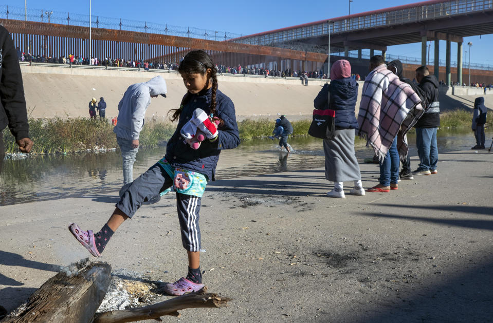 A migrant child tries to warm her feet with what remains of a campfire at the southern bank of the Rio Grande in Ciudad Juarez, Mexico, on Wednesday, Dec. 21, 2022. (AP Photo/Andres Leighton)