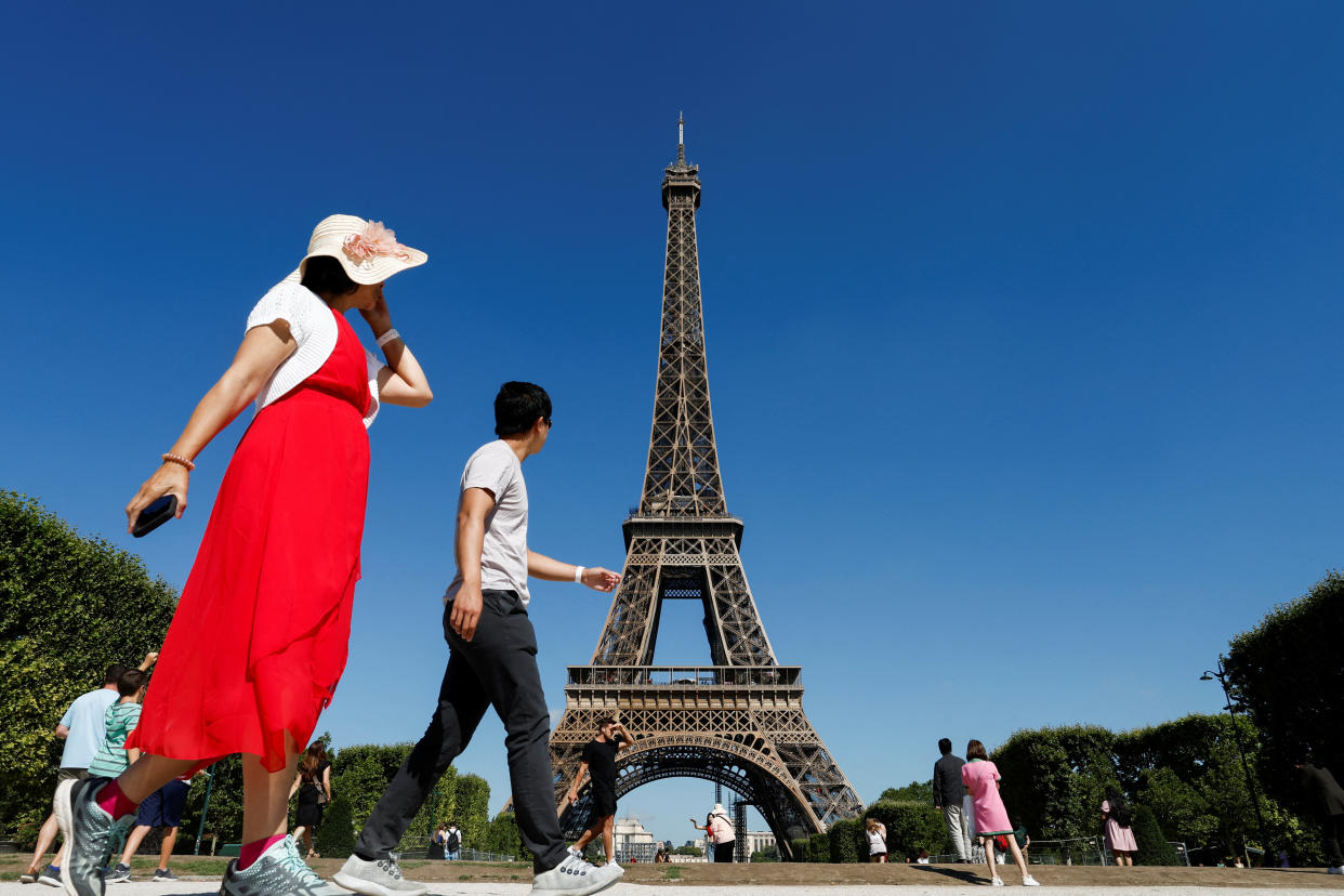 Tourists walk in front of the Eiffel tower during the 20th campaign of painting and stripping in Paris, France, July 5, 2022. REUTERS/Benoit Tessier