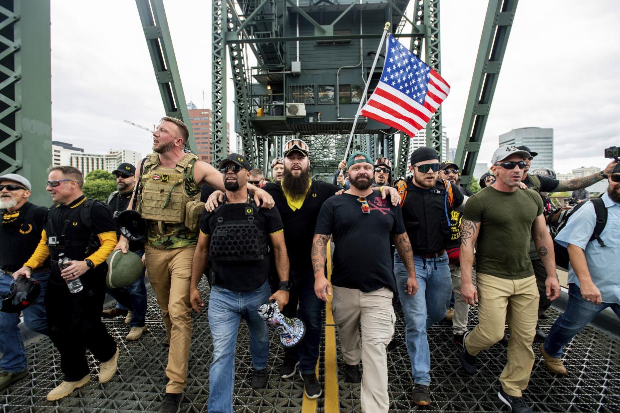 Organizer Joe Biggs, in green hat, and Proud Boys Chairman Enrique Tarrio, holding megaphone, march with members of the Proud Boys and other right-wing demonstrators march across the Hawthorne Bridge during a rally in Portland, Ore. 