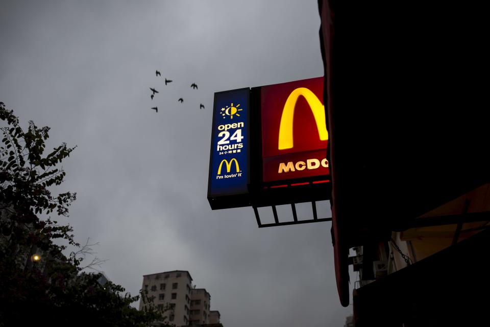 Birds fly past a sign of 24-hour McDonald's restaurant at sunrise in Hong Kong, China