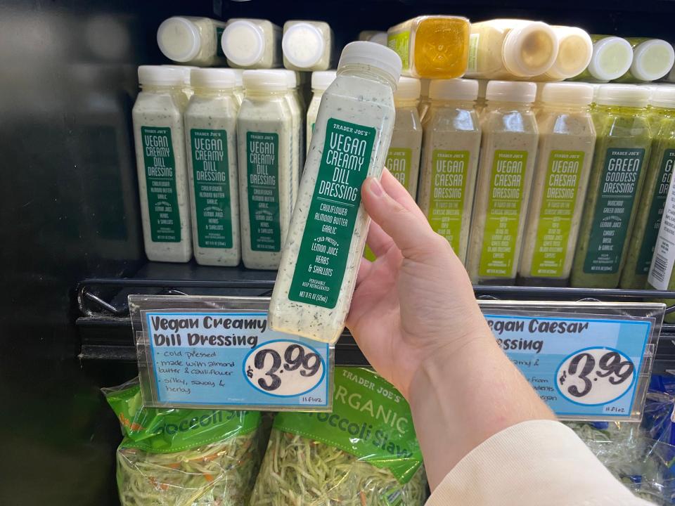 hand holding bottle of vegan dill dressing in front of a fridge of dressings at trader joes