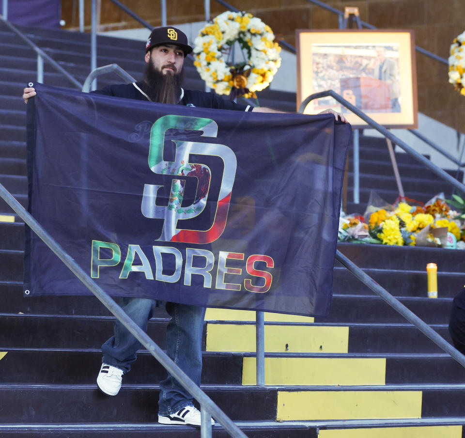 Guillermo Aguayo, of Spring Valley, holds up a Padres flag at a public memorial on the steps of Petco Park for Padres owner Peter Seidler, Tuesday, Nov. 14, 2023 in San Diego, Calif. The San Diego Padres announced Tuesday that Seidler has died. (K.C. Alfred/The San Diego Union-Tribune via AP)