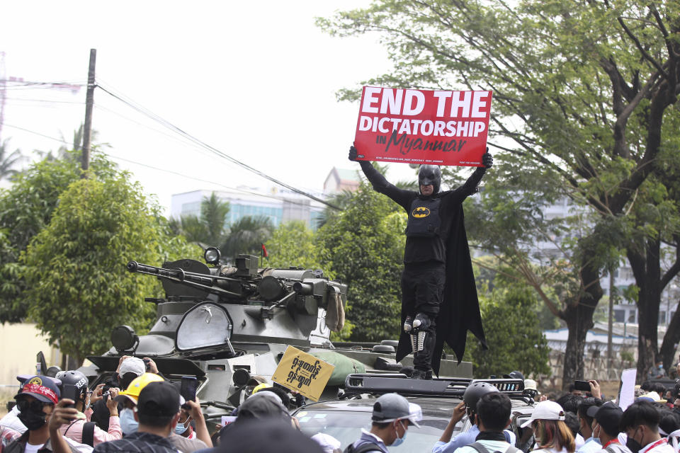 An anti-coup protester dressed in a Batman costume holds a sign that reads: "End the dictatorship in Myanmar" while standing on a vehicle parked next to an armored personnel carrier deployed outside the Central Bank of Myanmar building in Yangon, Myanmar, Monday, Feb. 15, 2021. Myanmar's military leaders have extended their detention of Aung San Suu Kyi, whose remand was set to expire Monday and whose freedom is a key demand of the crowds of people continuing to protest this month's military coup. (AP Photo)