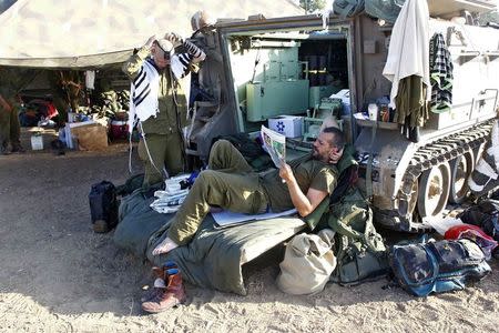 An Israeli soldier reads a newspaper as another one prepares to pray next to an armoured personnel carrier (APC) outside the southern Gaza Strip July 17, 2014. REUTERS/Ronen Zvulun