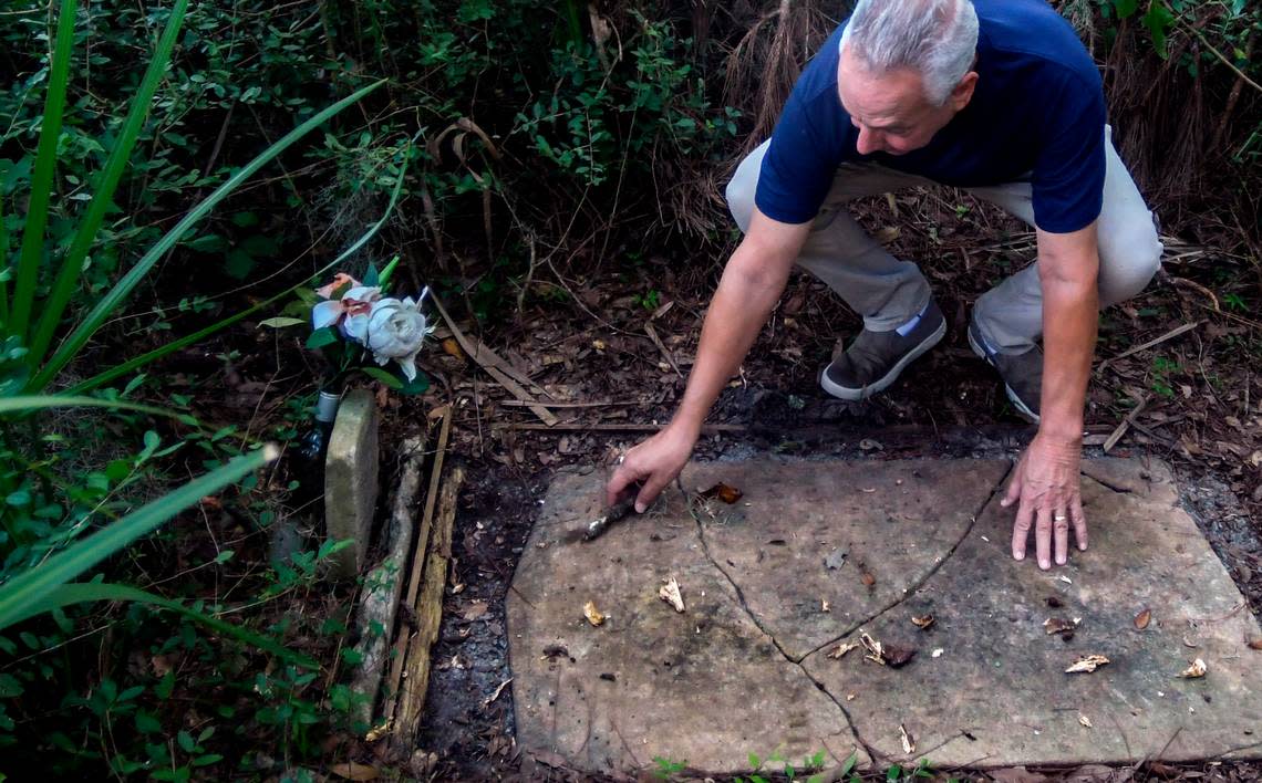 Cast in the shadow of the Cherry Hill Plantation live oak estimated to be more than 3 centuries old, Chuck Yahres clears debris from the grave marker of Mary Pope at the base of the tree on Sept. 21, 2022, in the town of Port Royal.