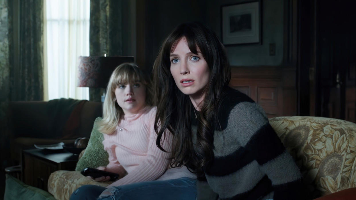  A still from the movie Malignant in which main character Madison Mitchell is sat in a living room with a little girl and looks scared. 