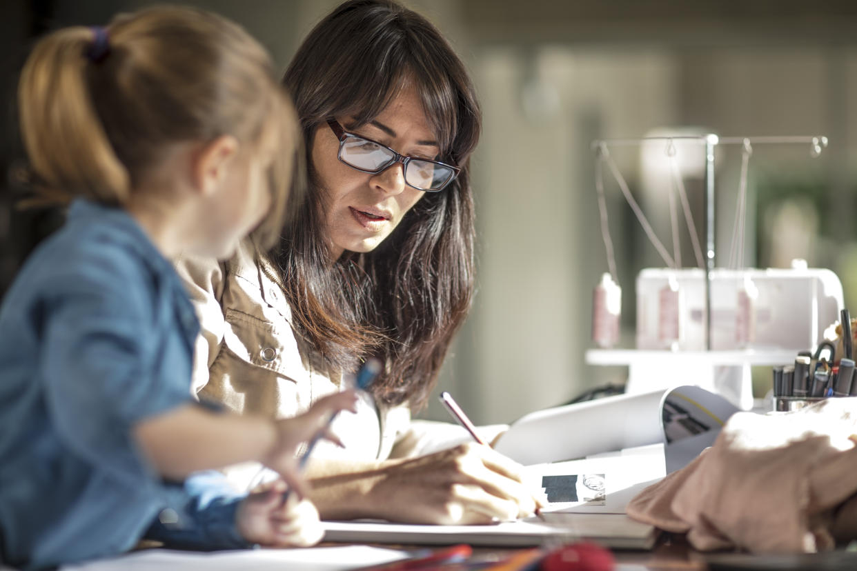 Mature woman doing paperwork while daughter drawing at table