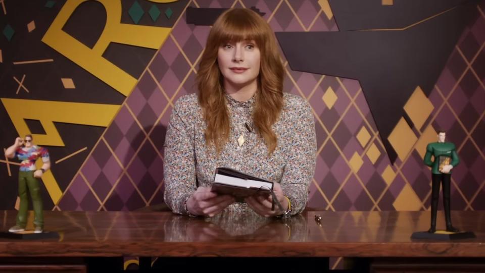 Red-haired Bryce Dallas Howard sits holding a book in Argylle