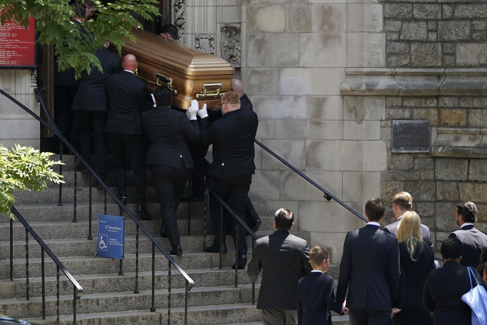 Pallbearers carry a gold casket into a church and people follow.