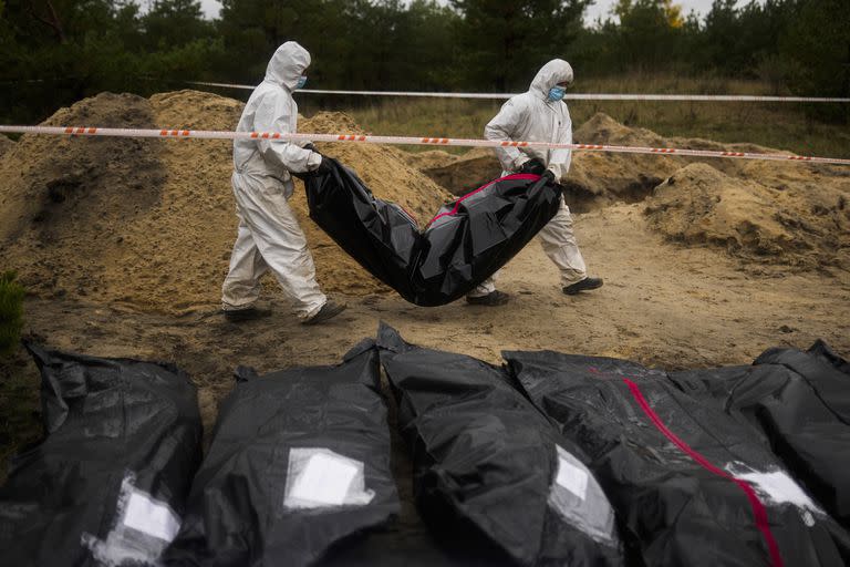 Miembros de un equipo forense cargan una bolsa para cadáveres mientras trabajan en el sitio de una fosa común, en Lyman, Ucrania