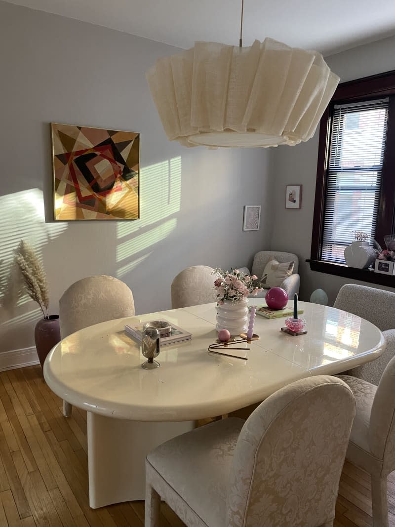 Oval modern white marble table with modern white fabric chairs, large pleated chandelier, geometric art