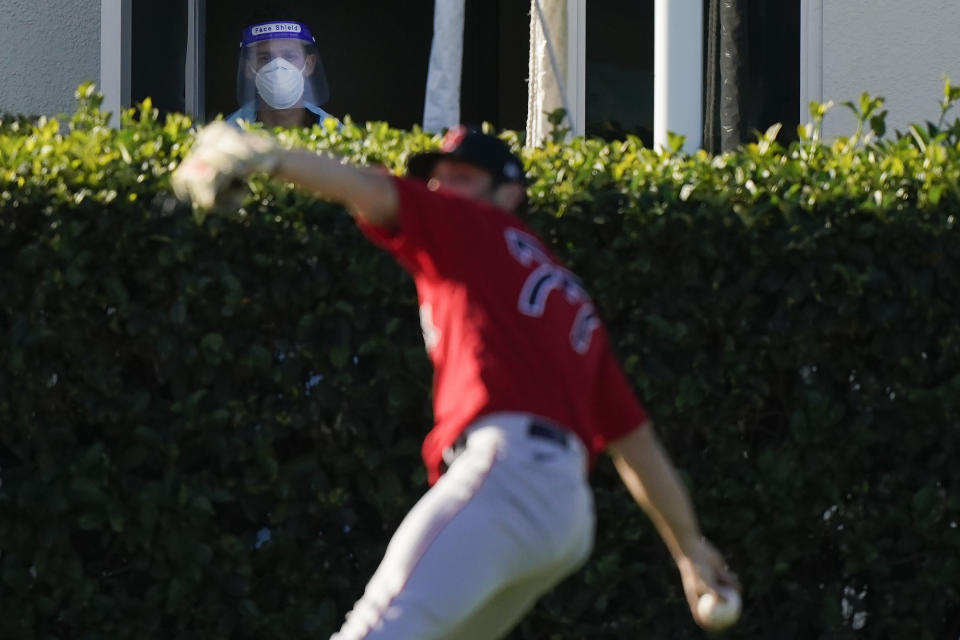 Boston Red Sox pitcher Jay Groome (77) throws the ball as a medical worker with a face shield near a testing site watches the players during spring training baseball practice on Monday, Feb. 22, 2021, in Fort Myers, Fla. (AP Photo/Brynn Anderson)