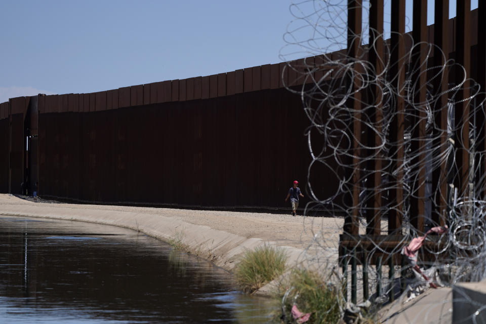 A man walks between a canal carrying water from the Colorado River and a border wall separating San Luis Rio Colorado, Mexico with San Luis, Ariz., on Sunday, Aug. 14, 2022, in San Luis Rio Colorado, Mexico. Steep water cuts to U.S. states using Colorado River water are looming, which means that Mexico could face more cuts, too. (AP Photo/Gregory Bull)