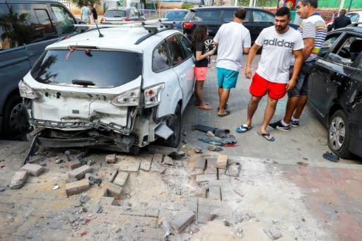 Israeli men stand next to a car that was damaged after a rocket fired by militants from the Gaza Strip fell in the southern Israeli town of Sderot on August 9, 2018